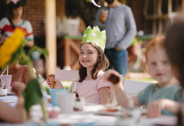 Group of small children sitting at the table outdoors on garden party, eating.