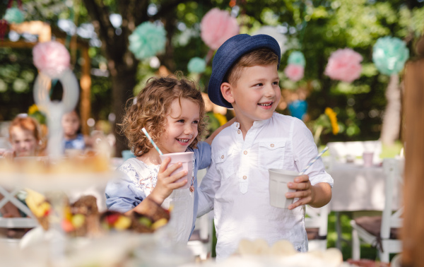 Small children standing outdoors in garden in summer, holding drinks. A celebration concept.