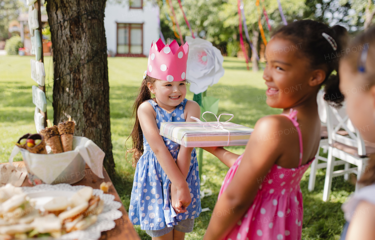 A portrait of small girl with friends and presents outdoors in garden in summer.