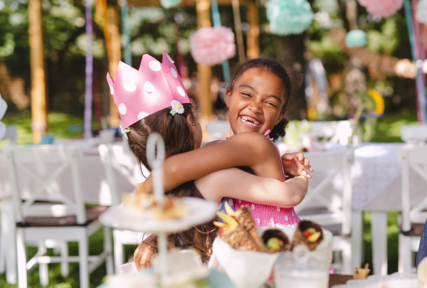 Small girls hugging outdoors in garden in summer, a birthday celebration concept.