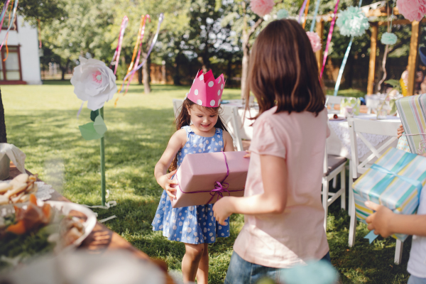 Small girls with hat outdoors in garden in summer, holding presents. A celebration concept.