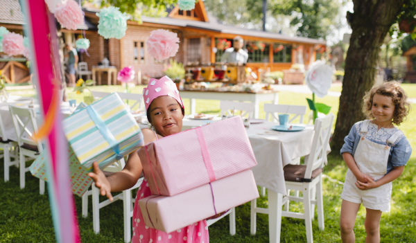 Portrait of small girl with a lot of presents outdoors in garden in summer.