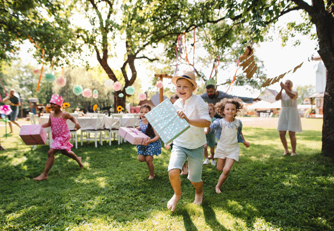 Small children running with present outdoors in garden on birthday party, playing.