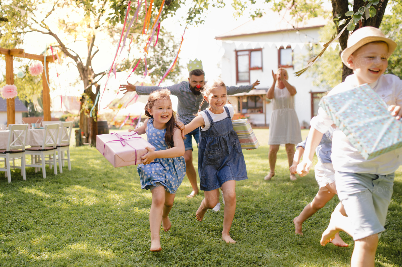 Small children ruunning with present outdoors in garden on birthday party, playing.