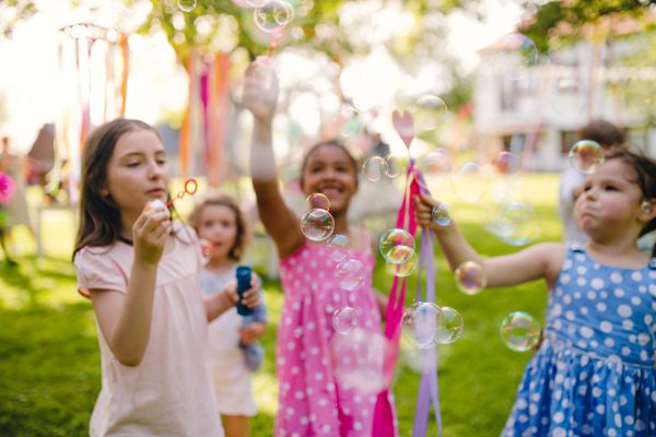 Small children standing outdoors in garden in summer, playing. A celebration concept.