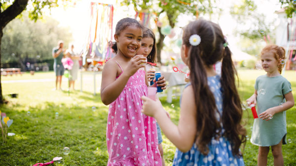 Small children standing outdoors in garden in summer, playing. A celebration concept.