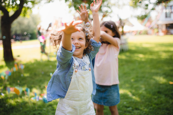 Small children standing outdoors in garden in summer, playing. A celebration concept.