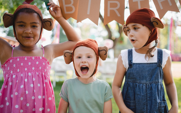 Small children with masks standing outdoors in garden in summer, playing. A celebration concept.