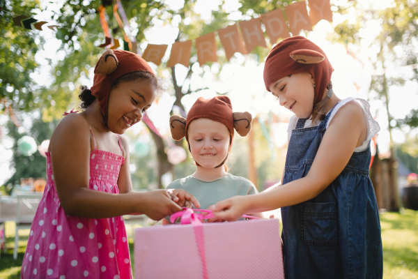 Small children with masks and present in box standing outdoors in garden in summer.