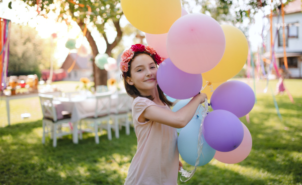 Small girl outdoors in garden in summer, playing with balloons. A celebration concept.