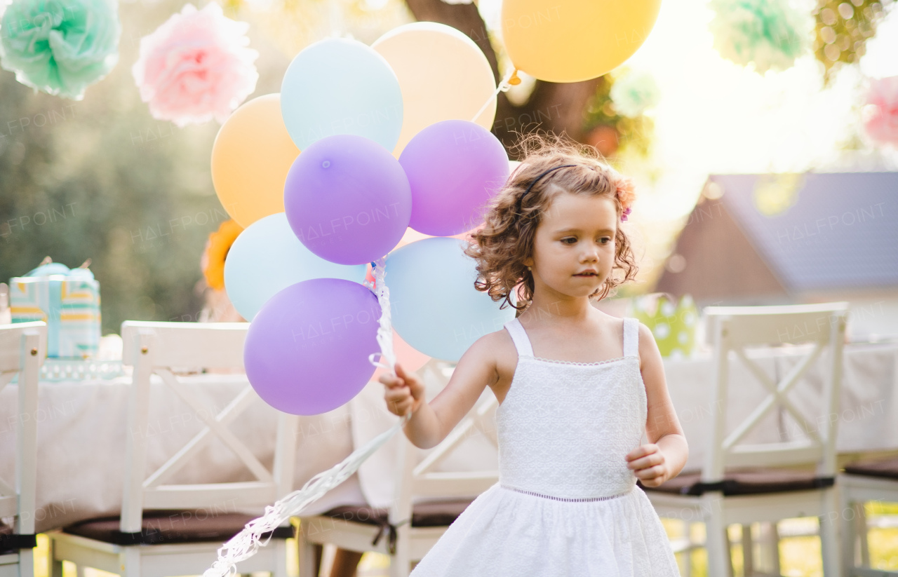 Portrait of happy small girl playing with balloons outdoors on garden party in summer.