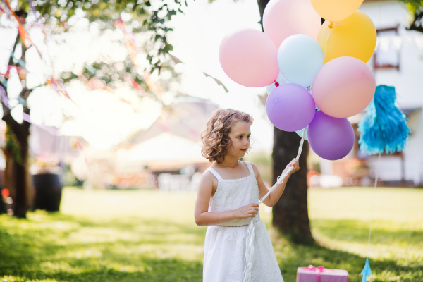 Small girl outdoors in garden in summer, playing with balloons. A celebration concept.