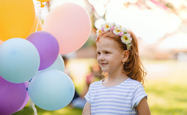 Small girl standing outdoors in garden in summer, birthday celebration concept.