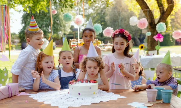 Down syndrome child with friends on birthday party outdoors in garden in summer.