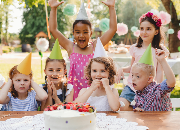 Down syndrome child with friends on birthday party outdoors in garden in summer.