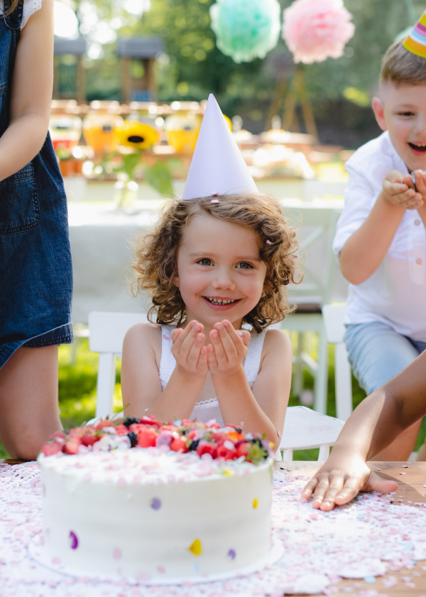 Front view of small girl with cake celebrating birthday outdoors in garden in summer, party concept.