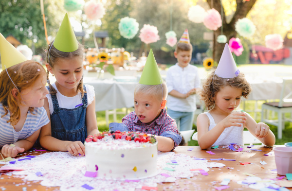 Down syndrome child with friends on birthday party outdoors in garden in summer.