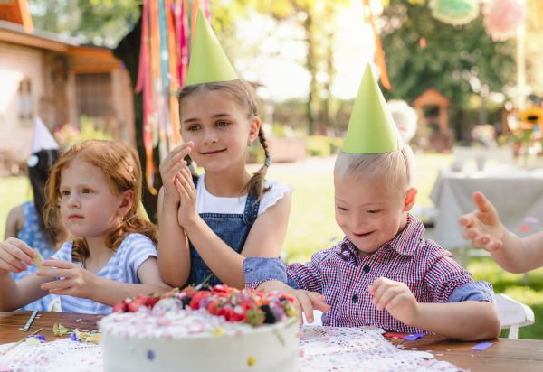 Down syndrome child with friends on birthday party outdoors in garden in summer.