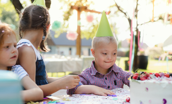 Down syndrome child with friends on birthday party outdoors in garden in summer.