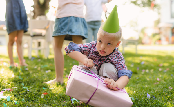 Down syndrome child with friends on birthday party outdoors in garden in summer, opening presents.