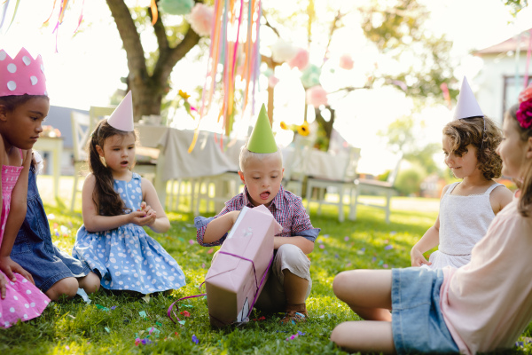 Down syndrome child with friends on birthday party outdoors in garden, opening presents.