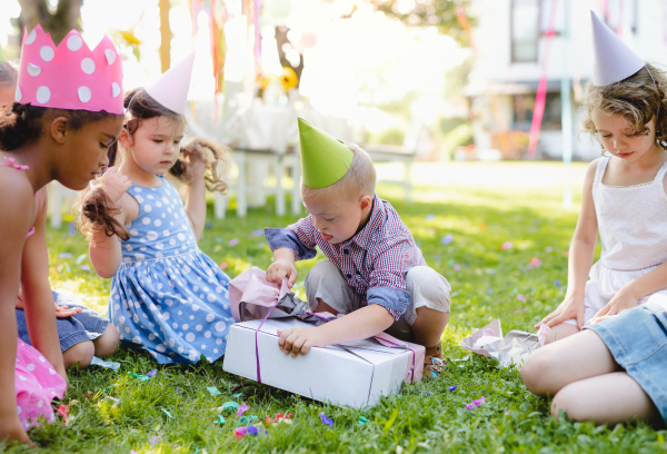 Down syndrome child with friends on birthday party outdoors in garden, opening presents.