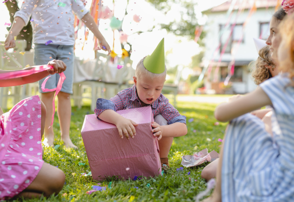 Down syndrome child with friends on birthday party outdoors in garden, opening presents.