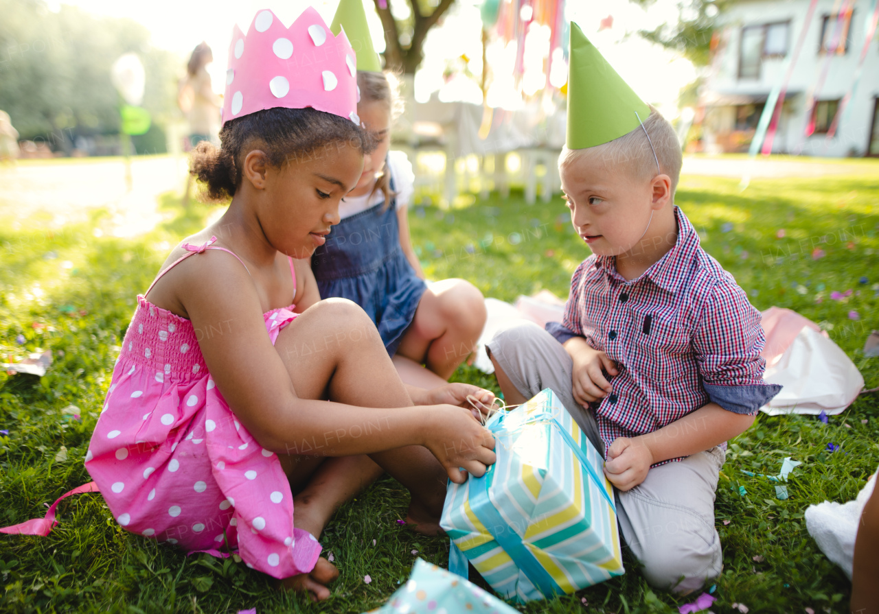 Down syndrome child with friends on birthday party outdoors in garden, opening presents.