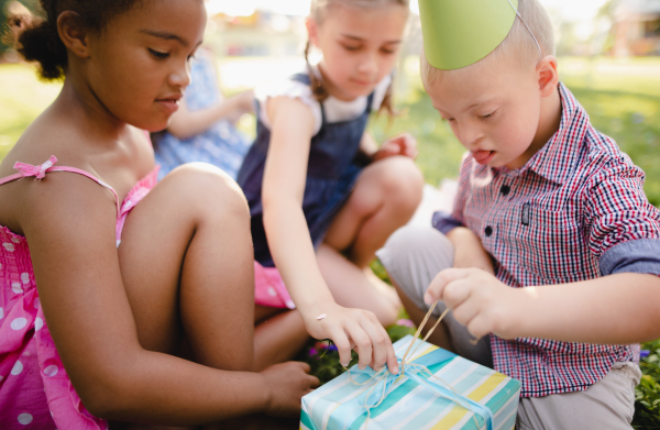 Down syndrome child with friends on birthday party outdoors in garden, opening presents.