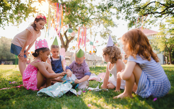 Down syndrome child with friends on birthday party outdoors in garden in summer, opening presents.