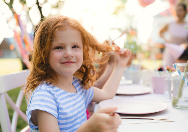 Small girl sitting outdoors in garden in summer, birthday celebration concept.