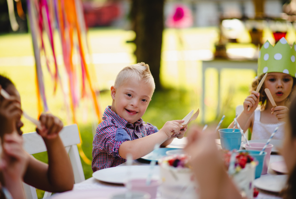 Down syndrome child with friends on birthday party outdoors in garden in summer.