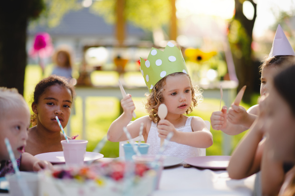 Group of small children sitting at the table outdoors on garden party, eating.