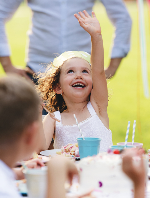 A happy small girl celebrating birthday outdoors in garden in summer, party concept.