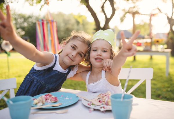 Happy small girls sitting at table on summer garden party, birthday celebration concept.