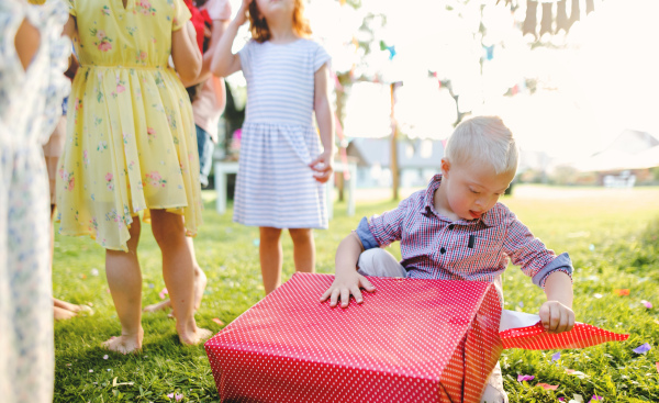 Down syndrome child with friends on birthday party outdoors in garden in summer, opening presents.