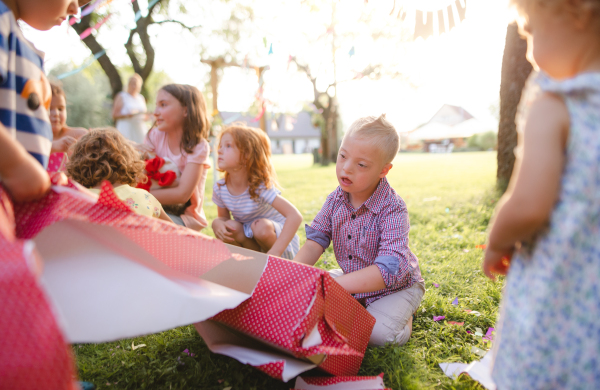 Down syndrome child with friends on birthday party outdoors in garden, opening presents.