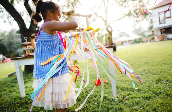 Small girl outdoors in garden in summer, playing with rainbow hand kite. A celebration concept.