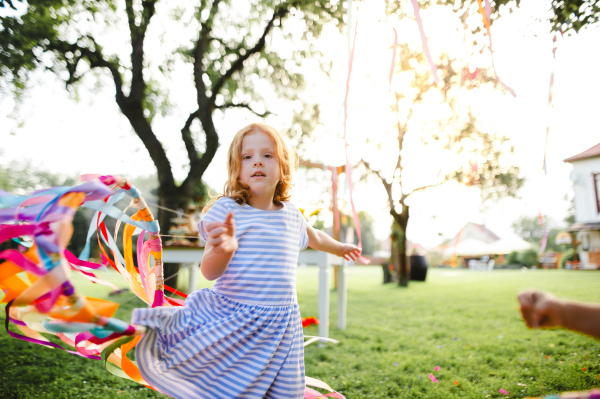 Small girl outdoors in garden in summer, playing with rainbow hand kite. A celebration concept.