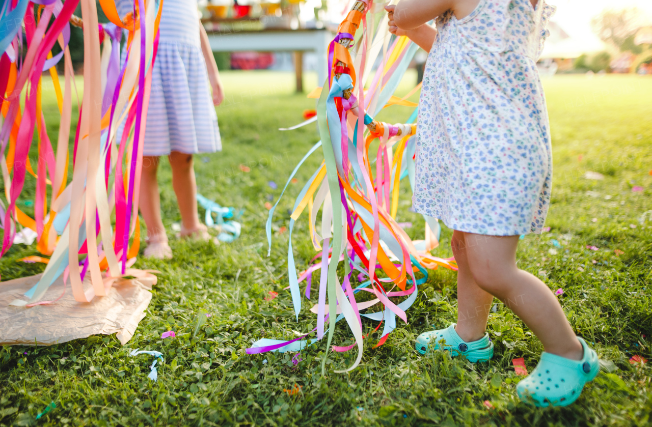 Unrecognizable small girls outdoors in garden in summer, playing with rainbow hand kite. A celebration concept.