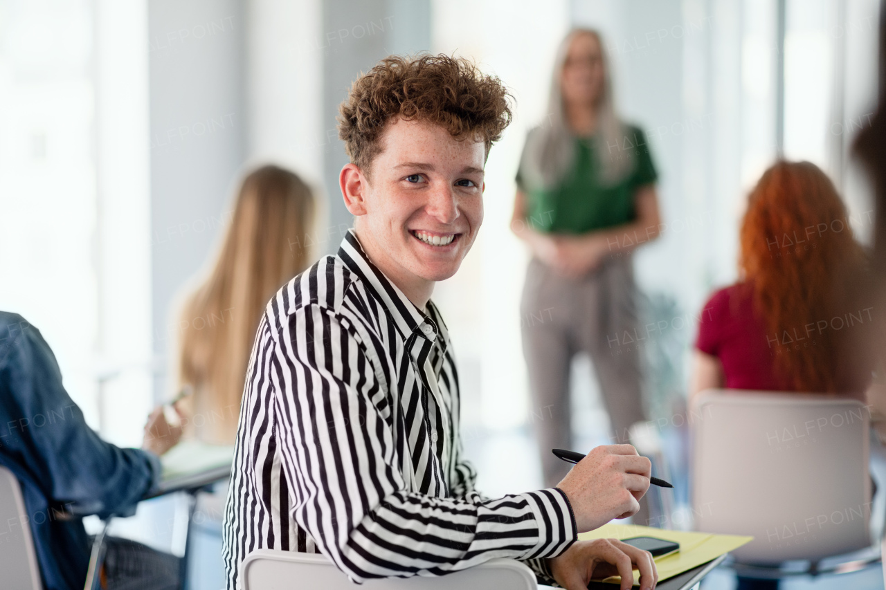 A portrait of young university student sitting in classroom indoors, looking at camera.