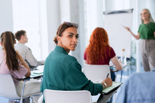 A portrait of young university student sitting in classroom indoors, looking at camera.