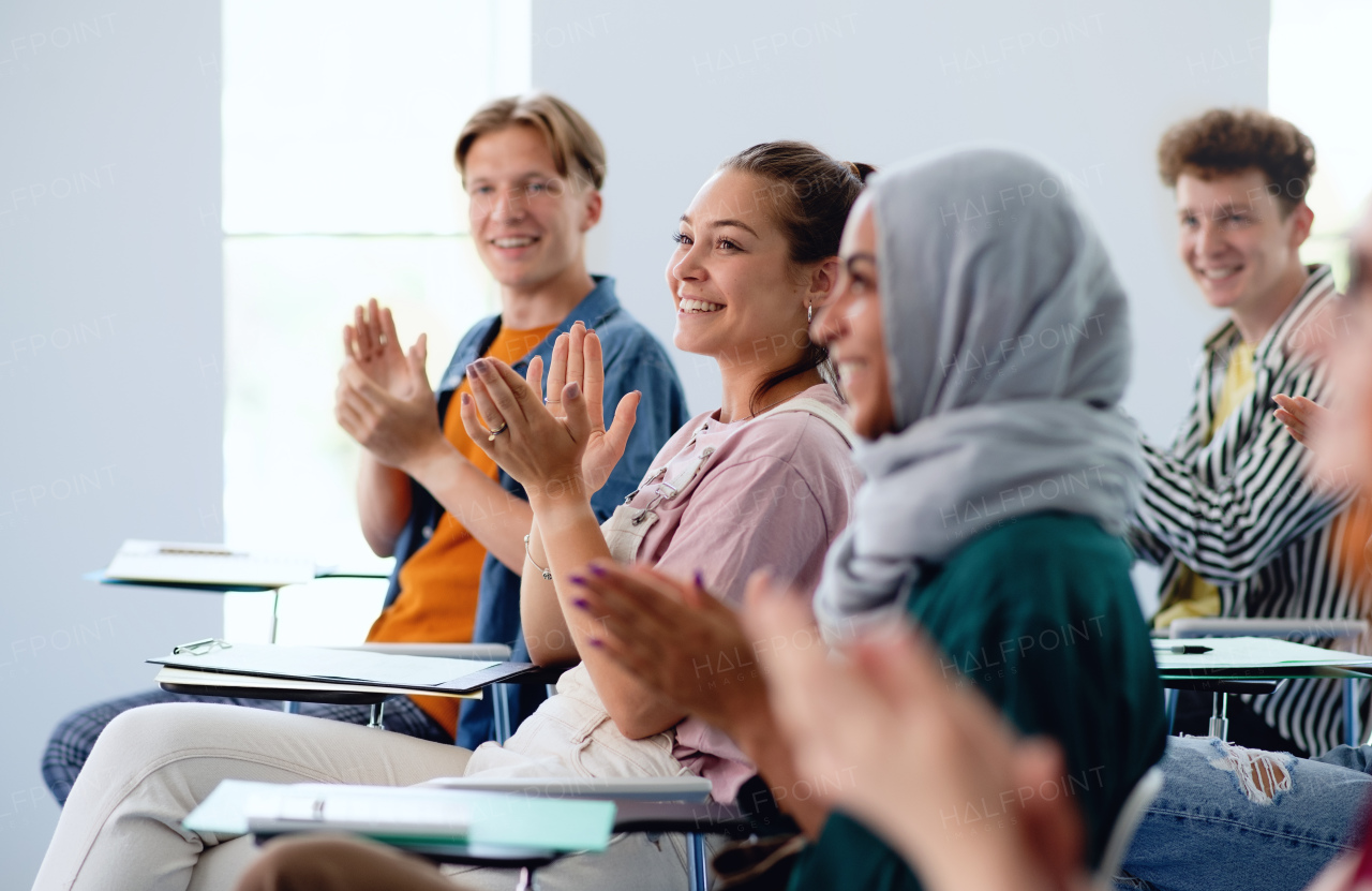 A portrait of cheerful university student sitting and studying in classroom indoors, clapping.