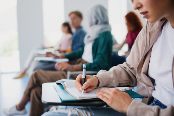 A group of unrecognizable university students sitting in classroom indoors, studying.