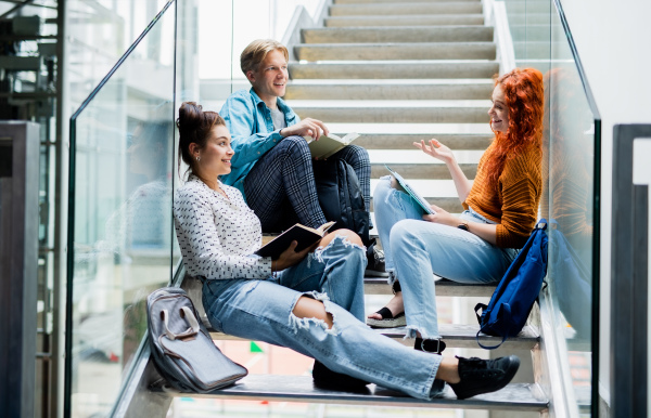 Cheerful university students sitting on stairs and talking indoors, back to school concept.