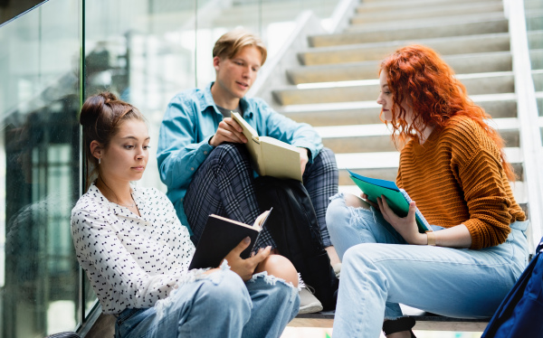 Cheerful university students sitting on stairs and talking indoors, back to school concept.