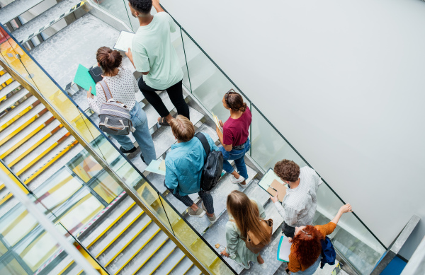 A top view of university students walking up the stairs indoors, looking at camera and waving.