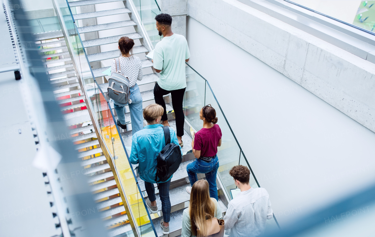 A rear view of university students walking up the stairs indoors, looking at camera and waving.