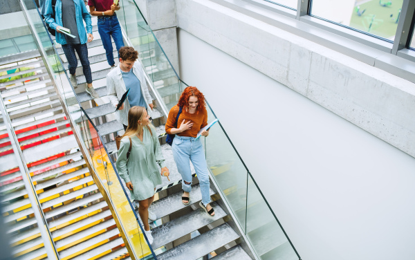 A top view of university students walking down the stairs indoors, talking.