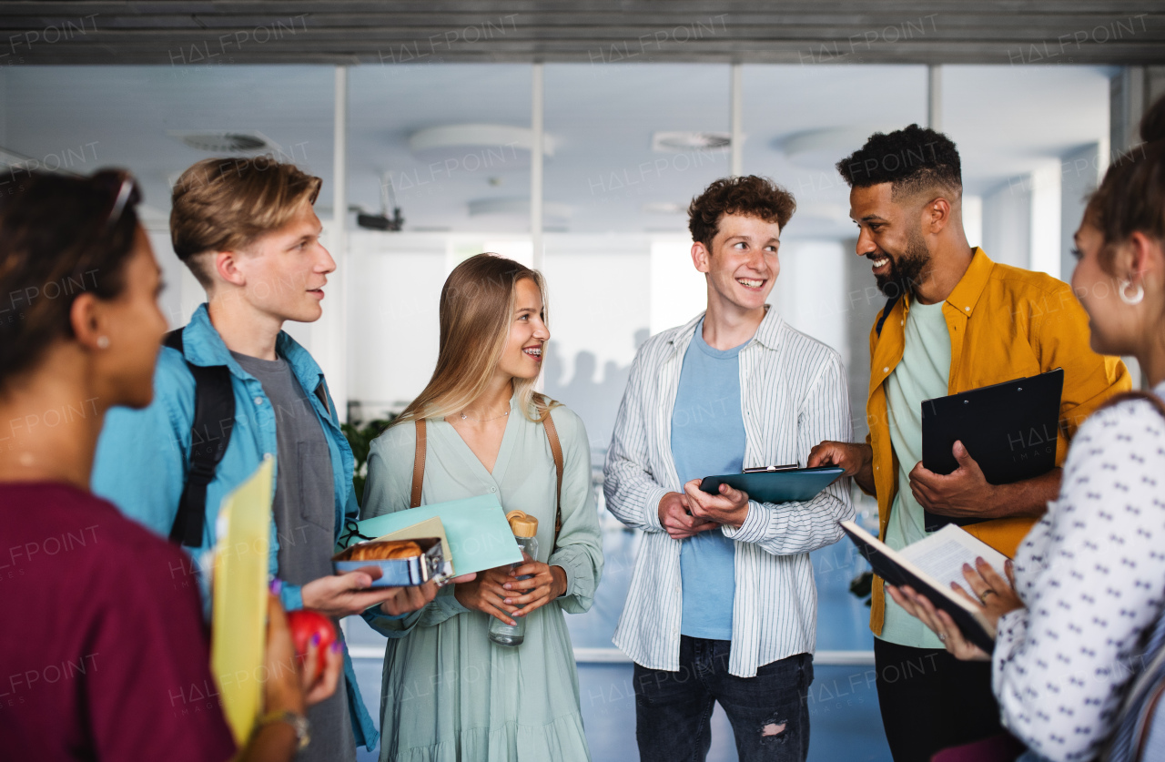 Group of cheerful university students standing in corridor indoors, talking.